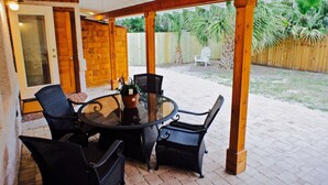 Un patio al aire libre con una mesa redonda y sillas, un ventilador de techo y una valla de madera al fondo.