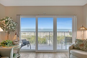 Una habitación con puerta de vidrio corredera que da a un balcón con vista a la playa y al océano.