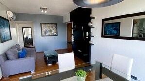 Una sala de estar moderna con una mesa de comedor de vidrio, sillas blancas, un sofá gris y una lámpara colgante grande.