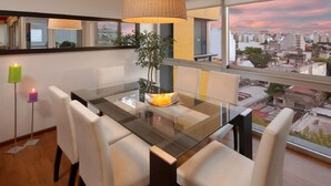 Un comedor moderno con una mesa de vidrio, sillas blancas y vistas a la ciudad.