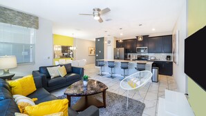 A modern living room with a sofa, coffee table, and a dining area with bar stools. - (NF4909) Home 4/3 Private Pool & Free Waterpark (Kissimmee)