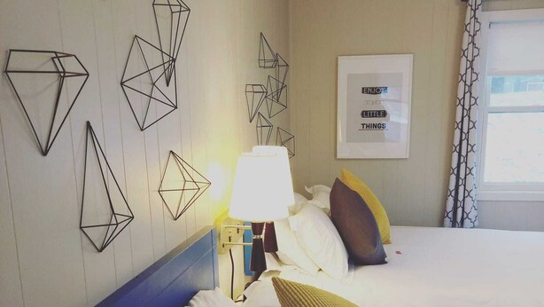 A hotel room with two beds, geometric wall art, a framed inspirational quote, and a window with curtains.