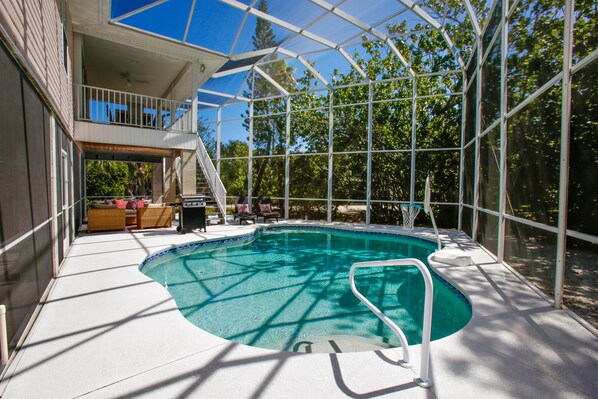 A swimming pool with a glass enclosure, surrounded by outdoor furniture and a covered patio area.