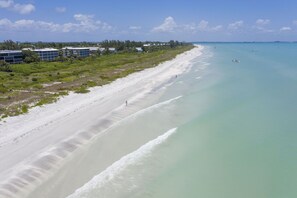 A coastal area with a sandy beach, a clear blue sea, and buildings in the background.