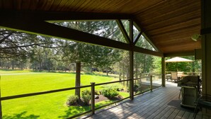 A covered deck with a view of a green field and trees. - 18 White Elm, 3 King Suites+Bunk Room! On 14th Green, Hot Tub, Bikes, 10 Passes (Sunriver)