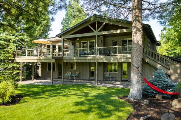 A two-story wooden house with a balcony, a covered patio, and a red hammock. - 18 White Elm, 3 King Suites+Bunk Room! On 14th Green, Hot Tub, Bikes, 10 Passes (Sunriver)