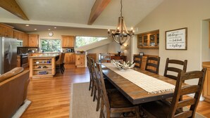 A spacious kitchen with wooden cabinets, a central island, and a dining area with a long table and chairs. - 18 White Elm, 3 King Suites+Bunk Room! On 14th Green, Hot Tub, Bikes, 10 Passes (Sunriver)