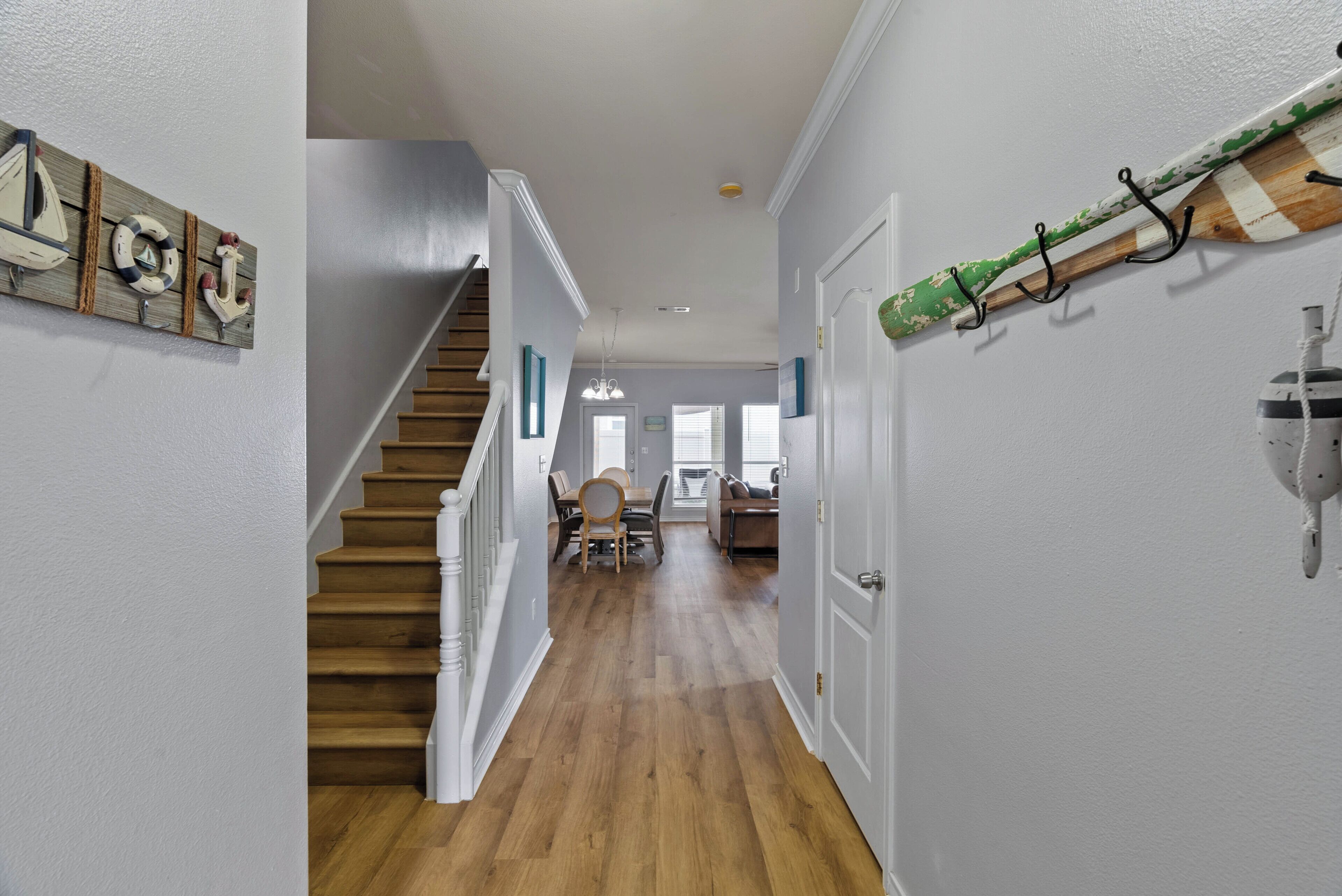 Un couloir avec un plancher en bois, un escalier et un coin repas comprenant une table et des chaises.