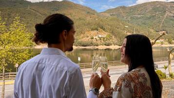 Deux personnes tenant des verres, avec une vue sur un lac et des collines en arrière-plan.