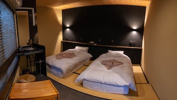 A room with two beds, a small wooden table, a sink, and a mirror.