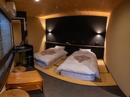 A room with two beds, a small wooden table, a sink, and a mirror.