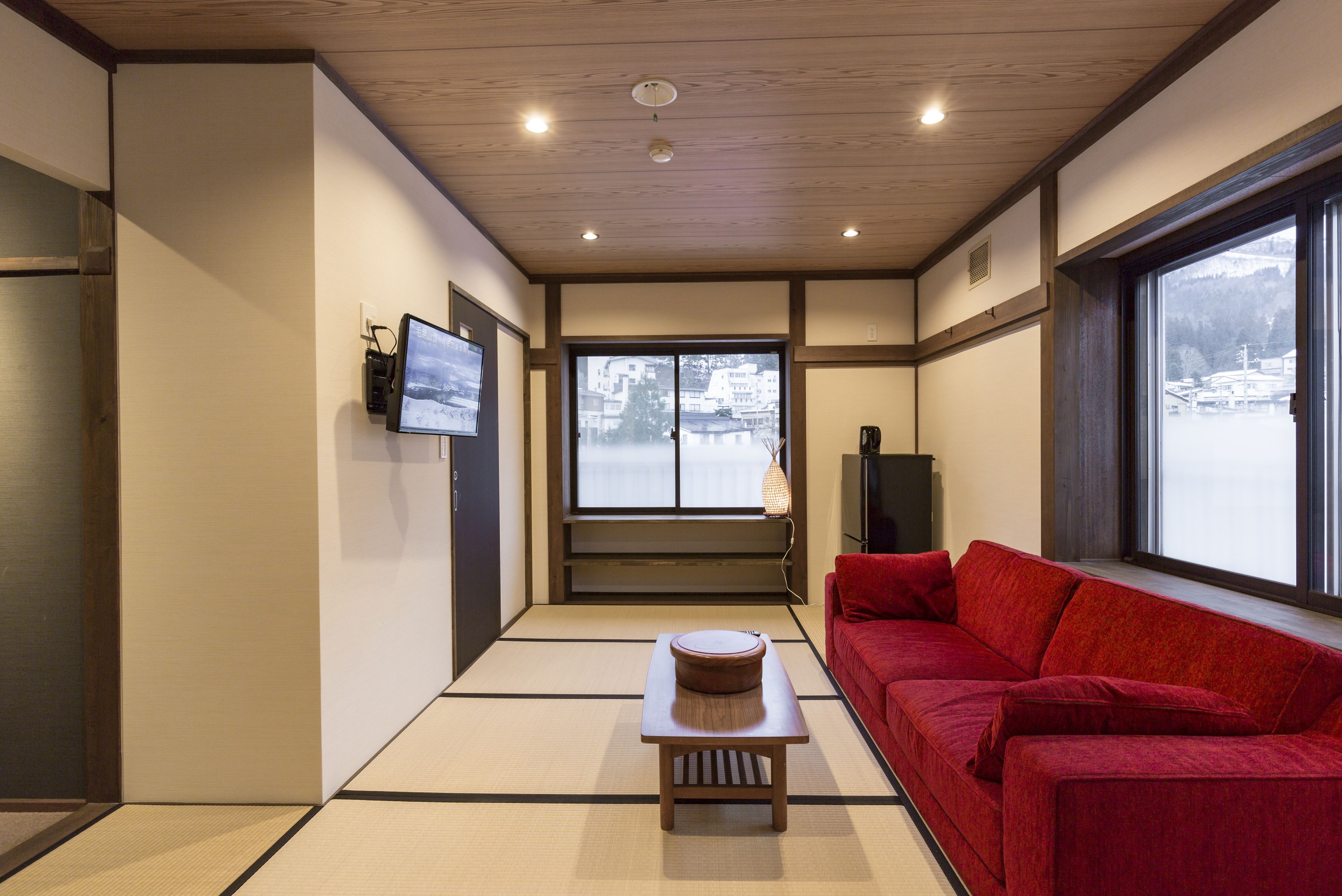 Een traditionele Japanse kamer met tatami vloeren, een rode bank, een houten tafel en een televisie aan de muur.