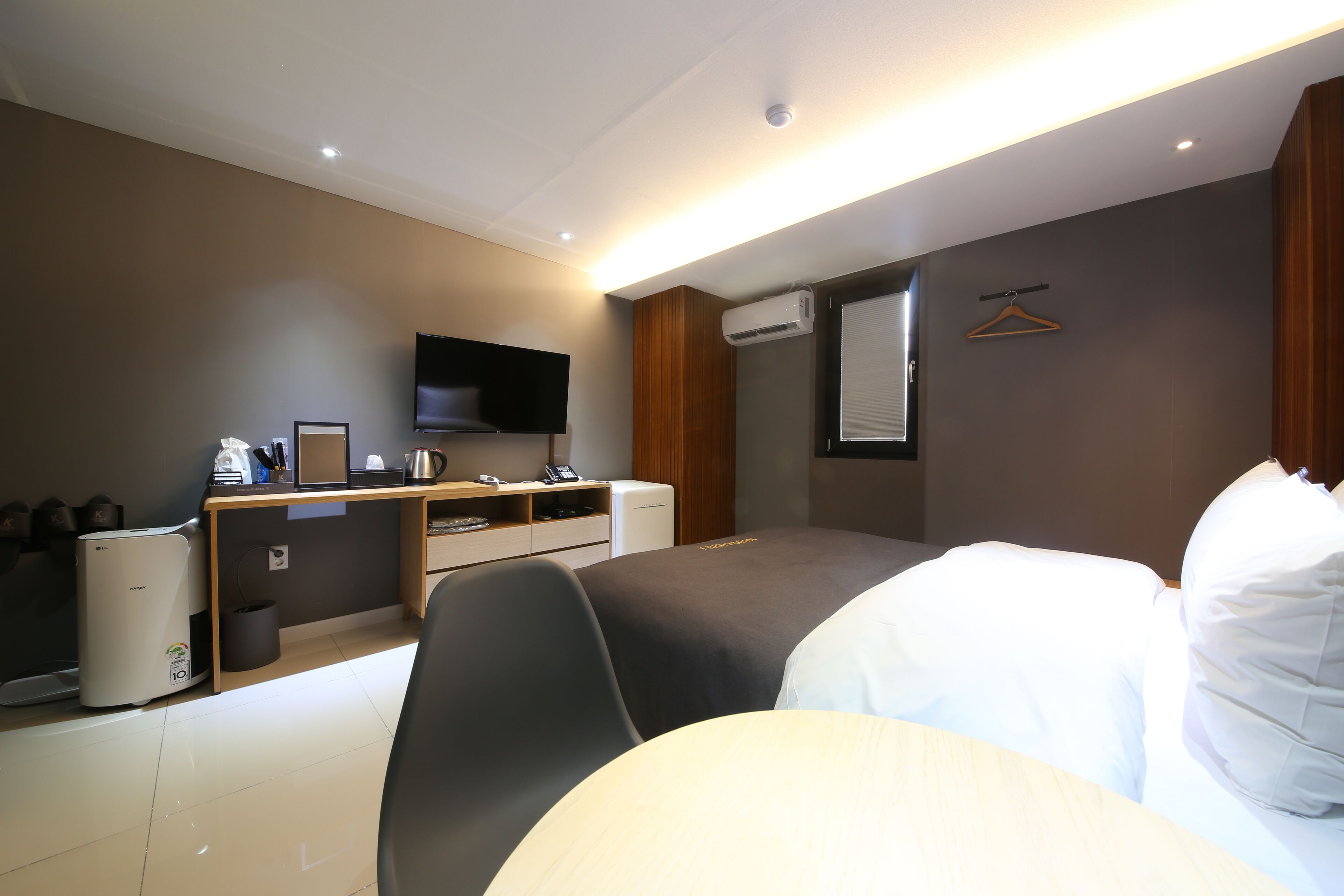 A hotel room with a bed, a desk with a computer, a television, and an air conditioning unit.