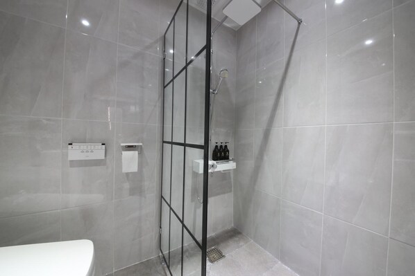 Un baño moderno con ducha envuelta en vidrio, inodoro blanco y repisa con artículos de aseo.