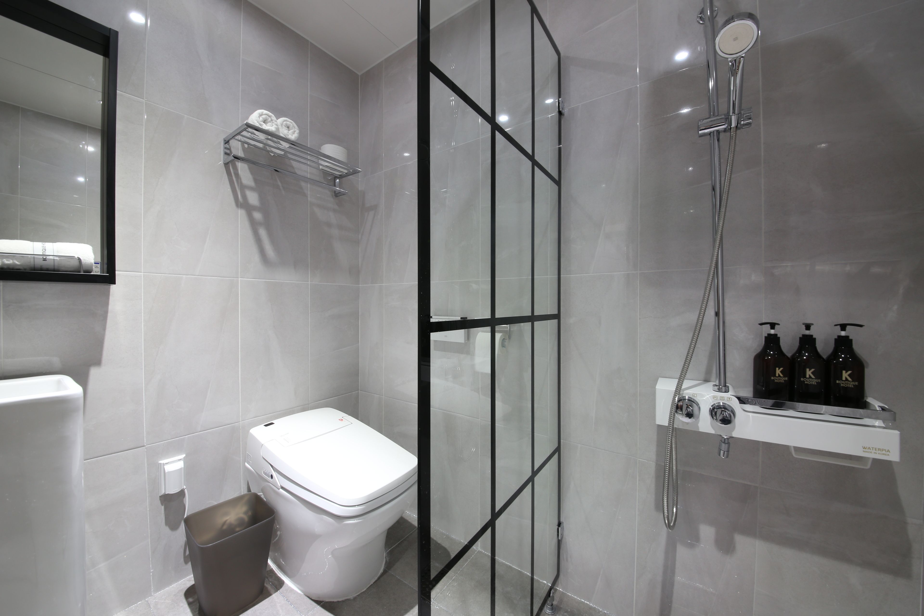 Un baño moderno con inodoro, ducha con mampara de vidrio y estante con artículos de aseo.