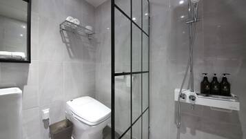 Un baño moderno con inodoro, ducha con mampara de vidrio y estante con artículos de aseo.