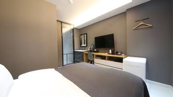 A hotel room with a bed, a desk, a chair, a TV, and a wardrobe.