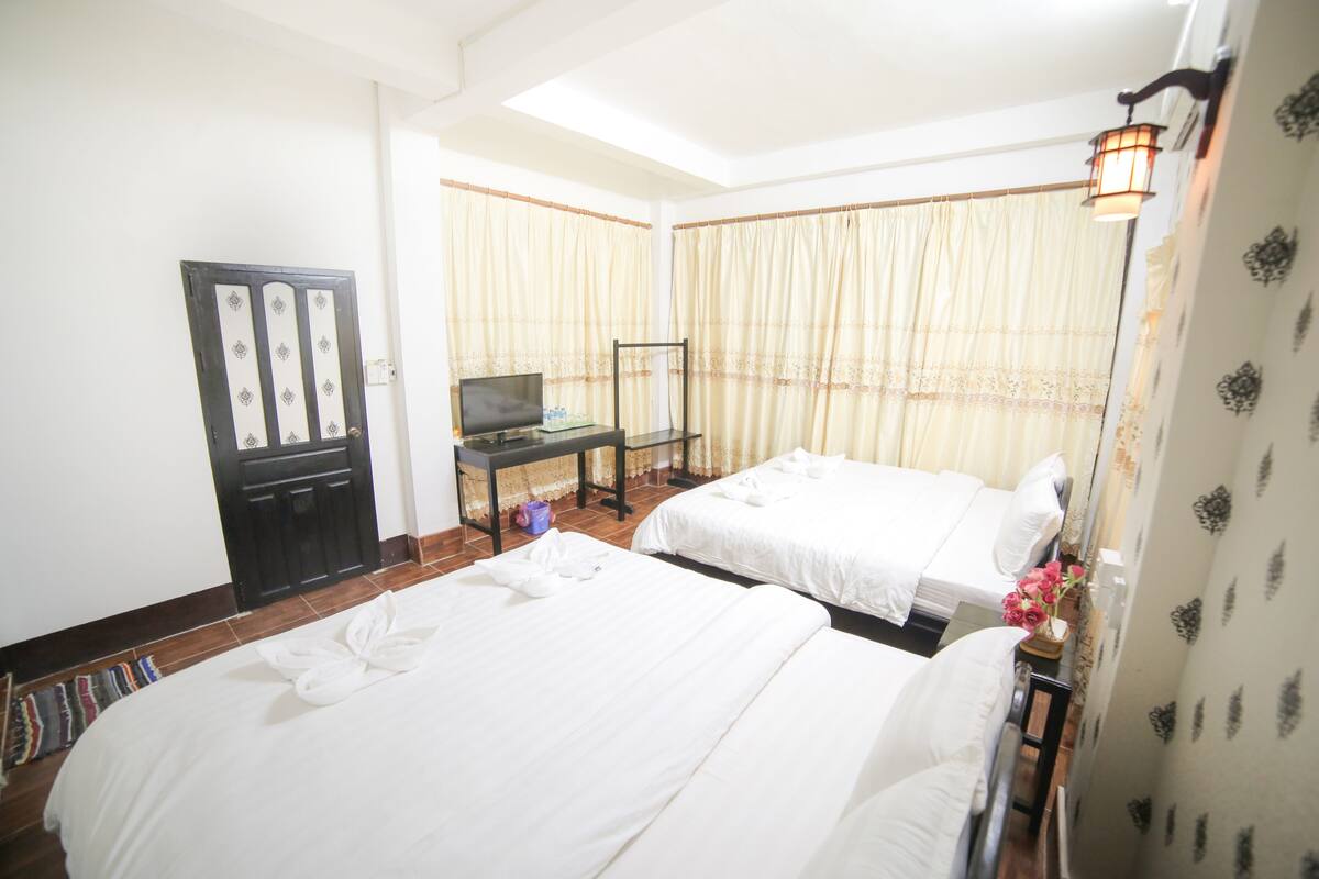 A hotel room with two beds, a desk with a television, and a door with decorative panels.