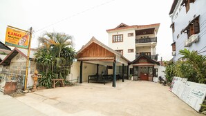 A courtyard with a covered seating area, a signboard, and a building with a balcony. - Maylay Guesthouse (Vang Vieng)