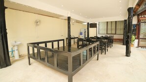 A spacious room with multiple tables and chairs, a sink, and a fan on the wall. - Maylay Guesthouse (Vang Vieng)