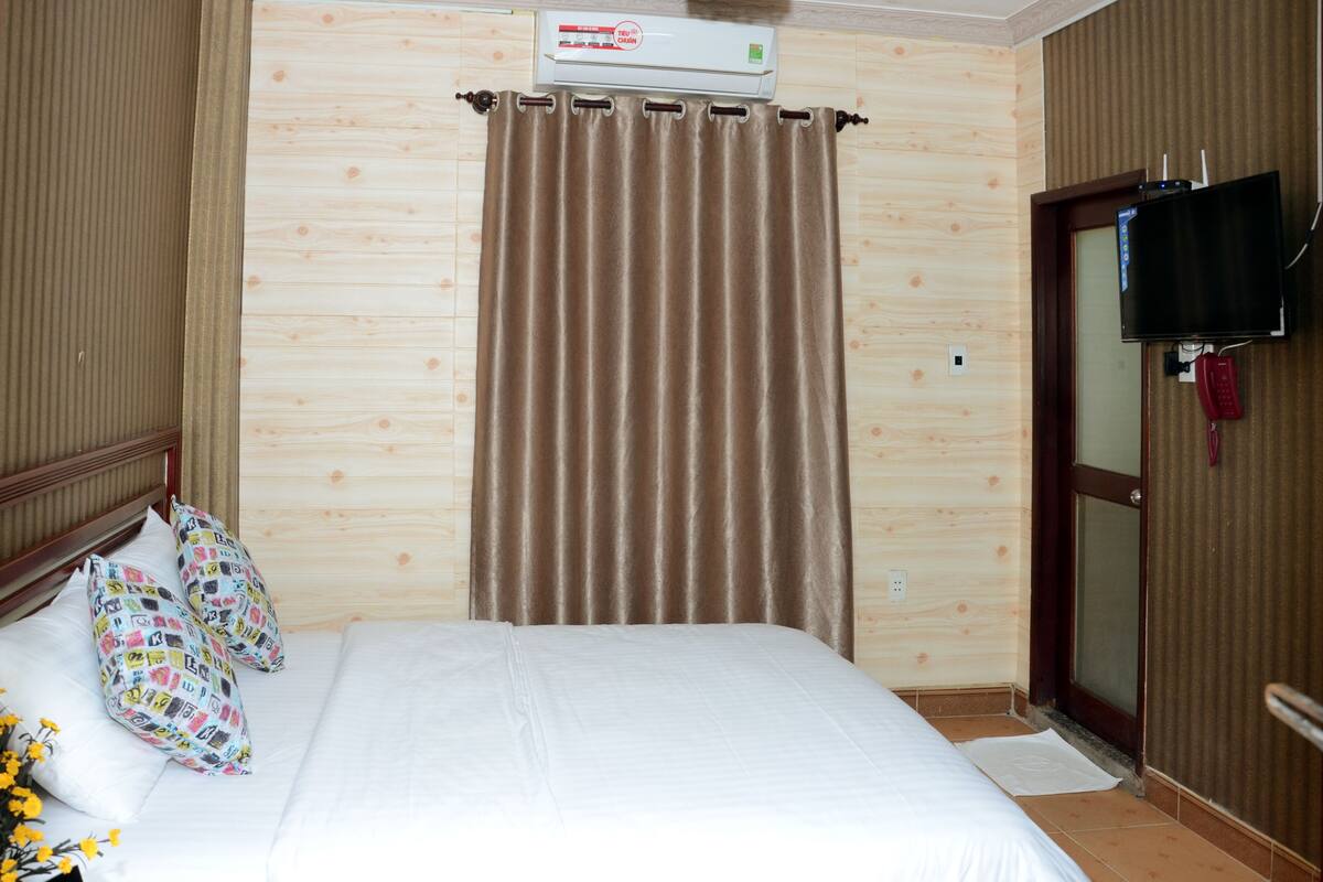 A hotel room with a bed, curtains, a television, and a telephone.