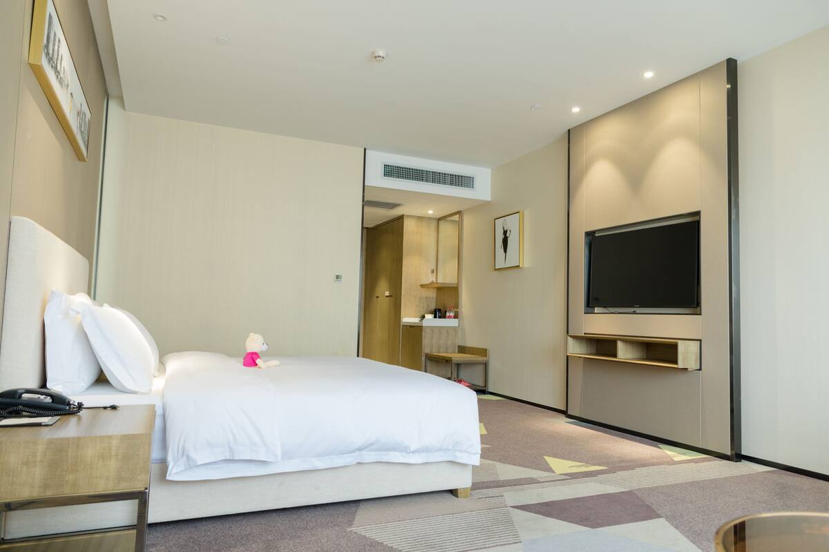 A hotel room with a bed, a desk, a chair, a television, and a mirror.