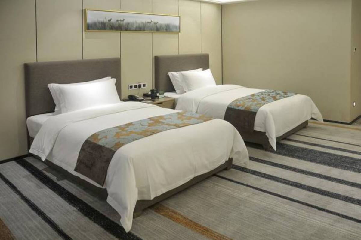 A hotel room with two beds, a striped carpet, and a painting on the wall.