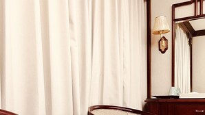 Una habitación con dos sillones tapizados, una mesita de madera con un libro, un espejo y una lámpara sobre un aparador de madera.