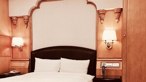 Una habitación de hotel con una cama grande, cabecero de madera, dos mesitas de noche con lámparas y un armario.