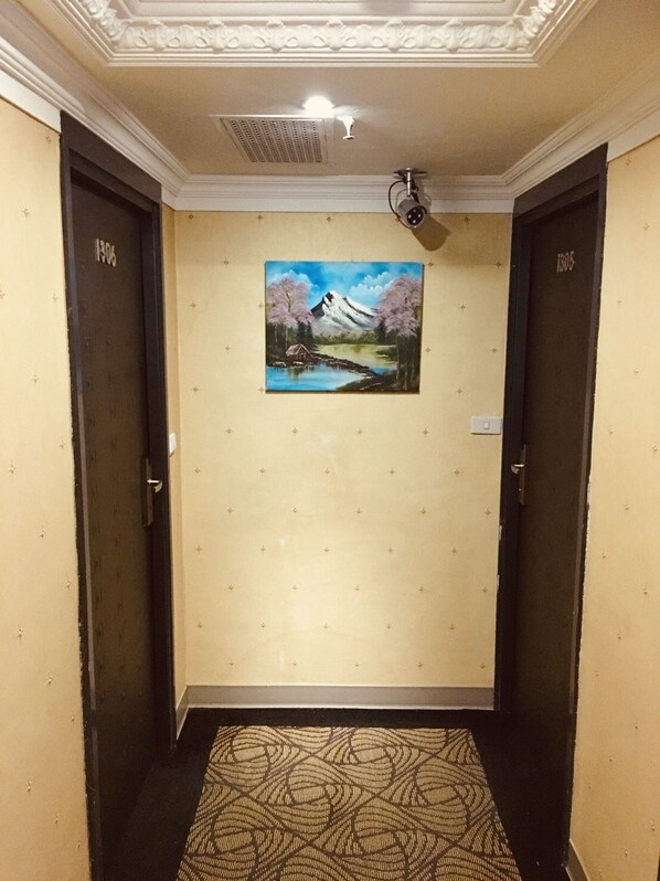 A hallway with two doors, a ceiling-mounted projector, and a painting of a mountain landscape. - Daxin Hotel (Taipei)