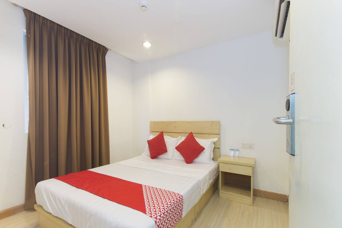Ein Hotelzimmer mit einem hölzernen Bett, roten und weißen Bettwäsche, einem Nachttisch und einem Fenster mit Vorhängen.