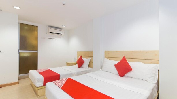 Habitación de hotel con dos camas, cada una con cabecero de madera, ropa de cama blanca y detalles en rojo.