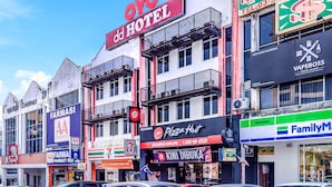 Un hotel con un letrero llamativo, negocios cercanos como una farmacia y Pizza Hut, y un estacionamiento con varios coches.