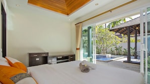 A hotel room with a bed, a TV, and a view of an outdoor pool area. - Oazza Villa (Rawai)