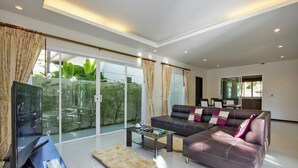 A modern living room with a large sectional sofa, a glass coffee table, and a flat-screen TV on a wooden stand. - Oazza Villa (Rawai)