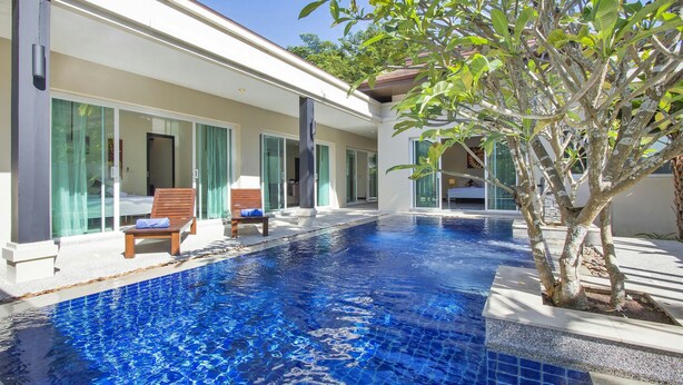 A swimming pool with a tiled edge, a wooden lounge chair, and a tree. - Oazza Villa (Rawai)