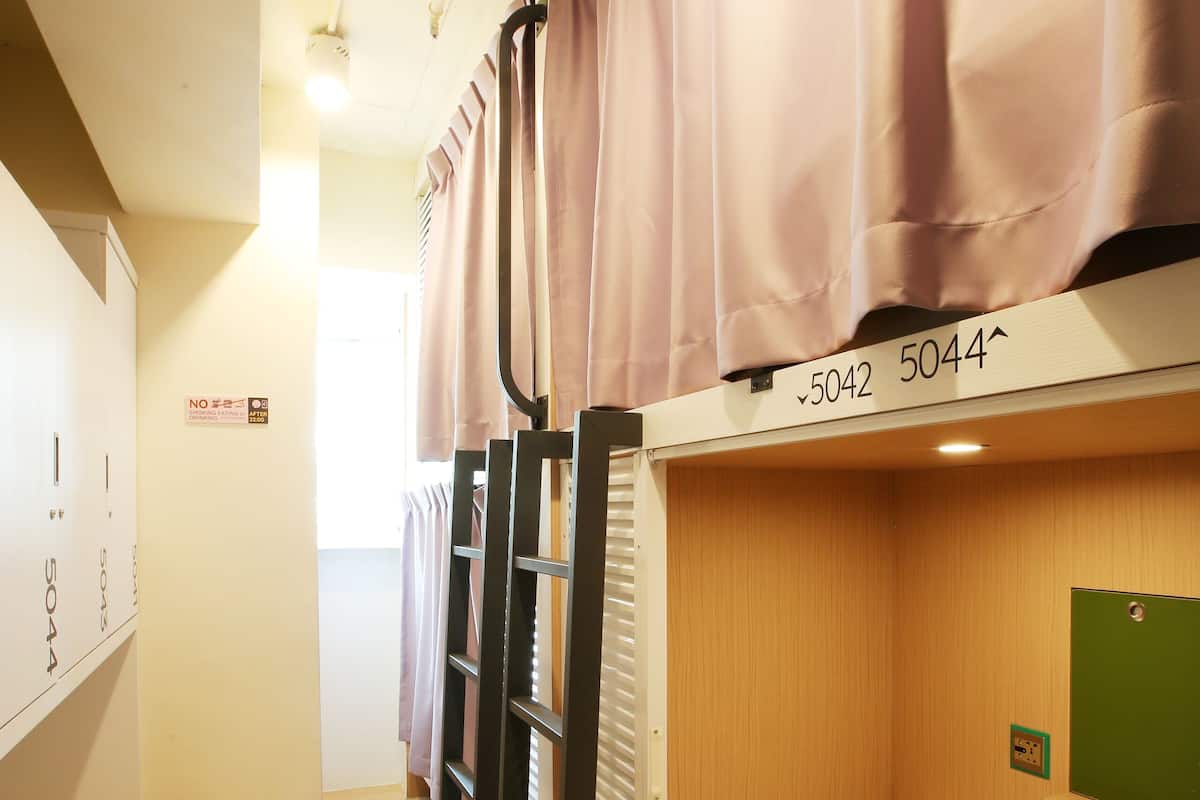 A dormitory room with bunk beds, a wooden floor, and a green bulletin board.