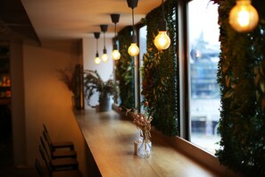 A restaurant interior with a long wooden counter, hanging light bulbs, and a vase with dried flowers. - Loosha Hostel (Taichung)