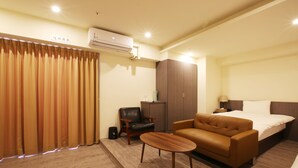 A hotel room with a bed, a sofa, a small table, a chair, an air conditioning unit, and a curtain. - Loosha Hostel (Taichung)