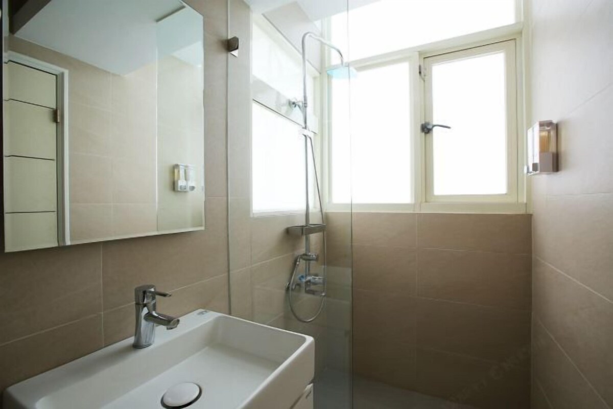 A bathroom with a sink, mirror, shower, and a window.