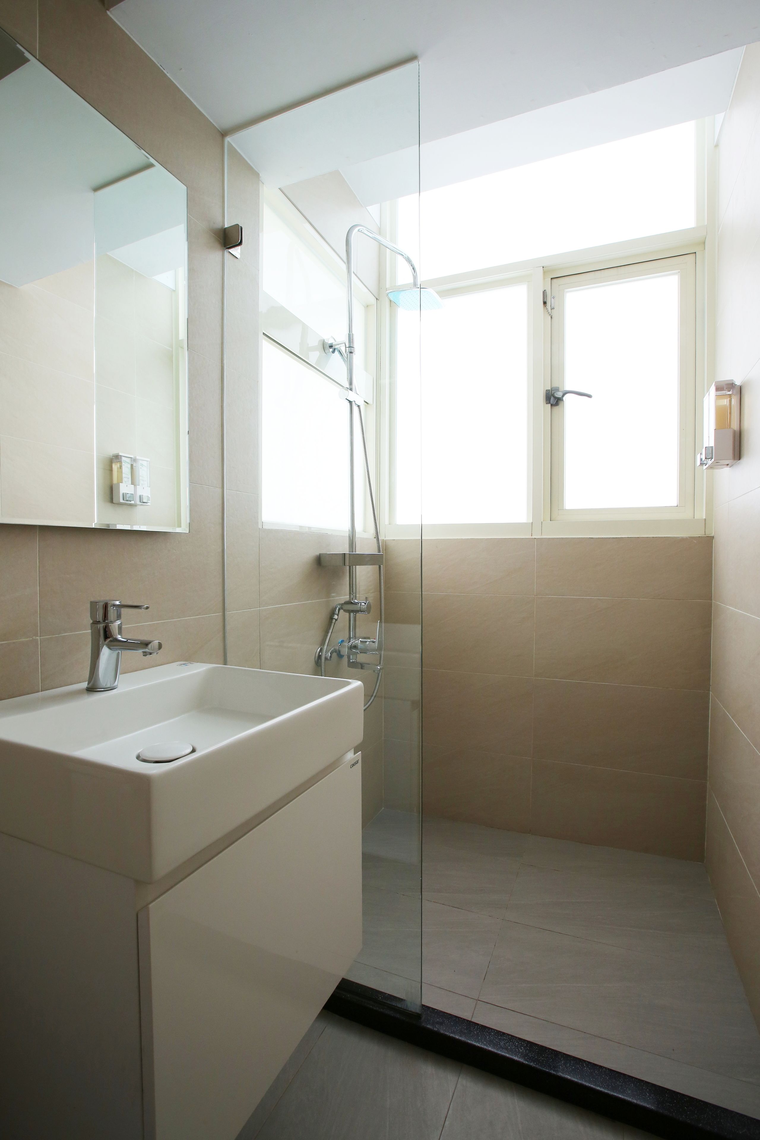 Un baño moderno con ducha de vidrio, un espejo grande y un lavamanos con grifo.