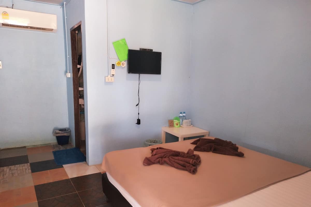 Una habitación de hotel con cama, una mesita de noche con artículos de tocador, un televisor montado en la pared y un mostrador de recepción.