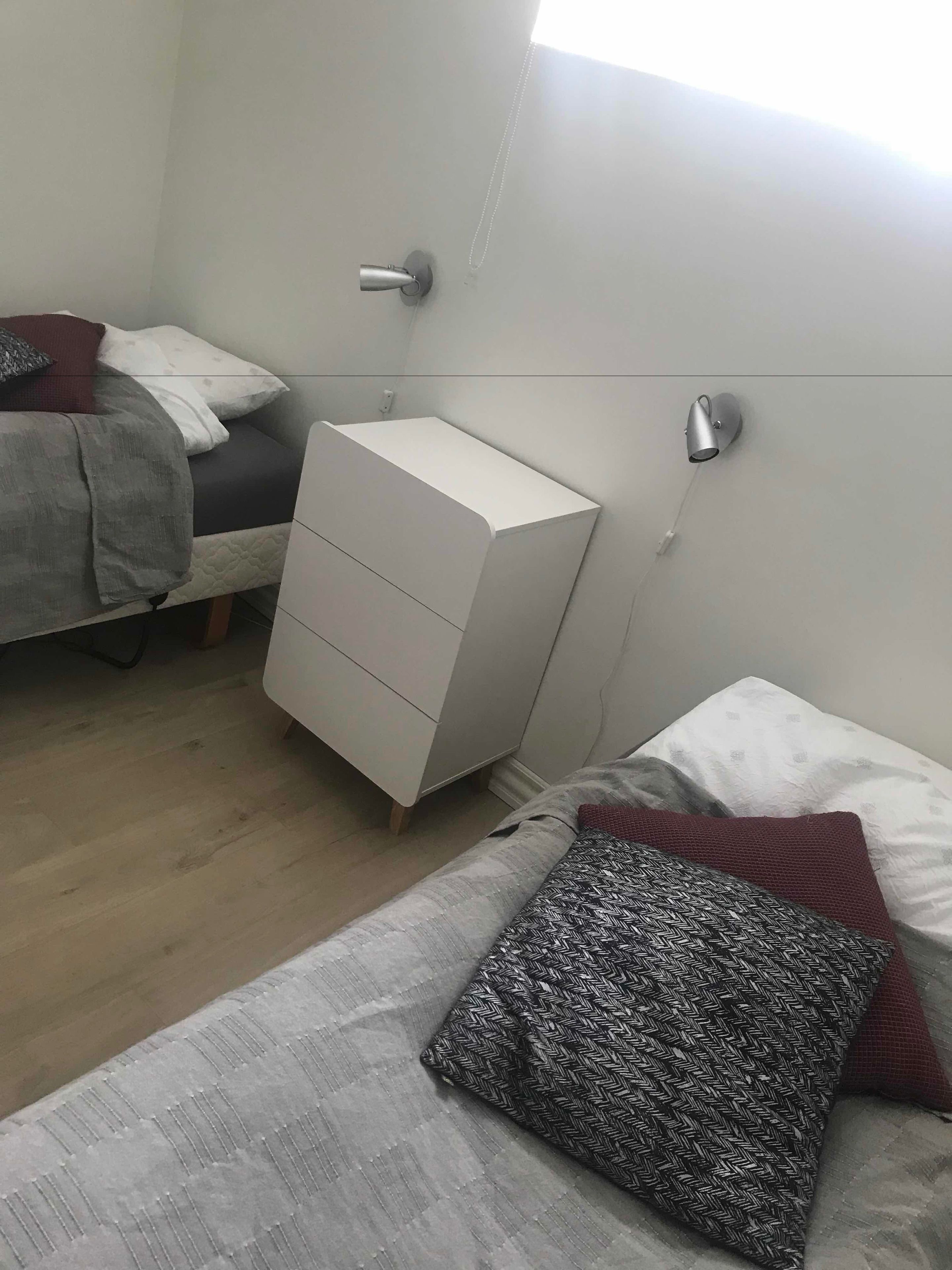 A bedroom with a bed, a bedside table, a dresser, and a wall-mounted lamp.