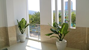 A room with two potted plants, a balcony with a view of buildings and greenery, and a window with a view of the cityscape. - Homestay 78 (Ho Chi Minh City)