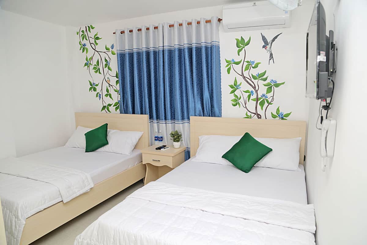 A hotel room with two beds, a nightstand, a TV, and a window with blue curtains.