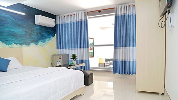 A hotel room with a bed, a desk with a computer, a small table with a plant, and a wardrobe. - Homestay 78 (Ho Chi Minh City)