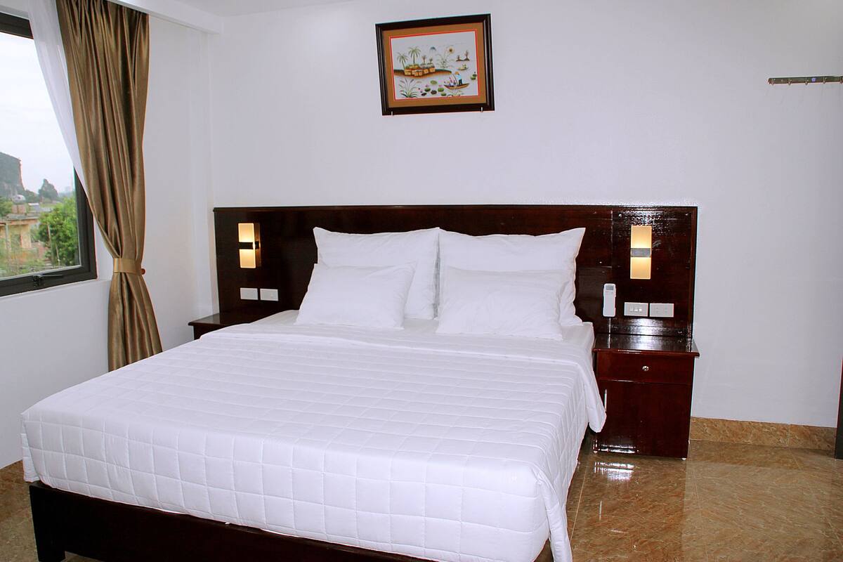 A neatly made bed with white bedding, a wooden headboard, two bedside tables with lamps, and a framed picture on the wall.