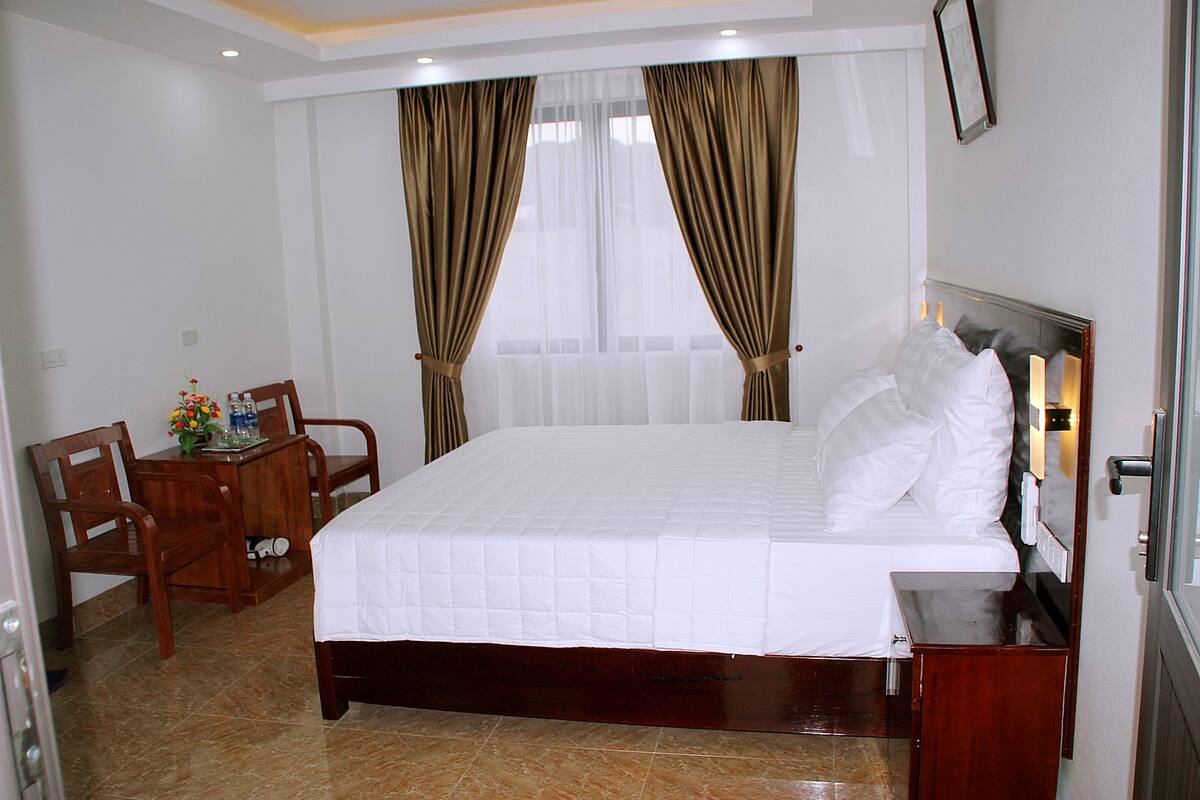 A hotel room with a large bed, a wooden desk with a chair, and a small table with a vase of flowers.