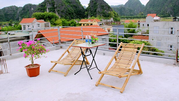 A rooftop terrace with two wooden lounge chairs, a small table, and a potted plant. - Tam Coc Victoria Hotel (Nam Hoa Lu)