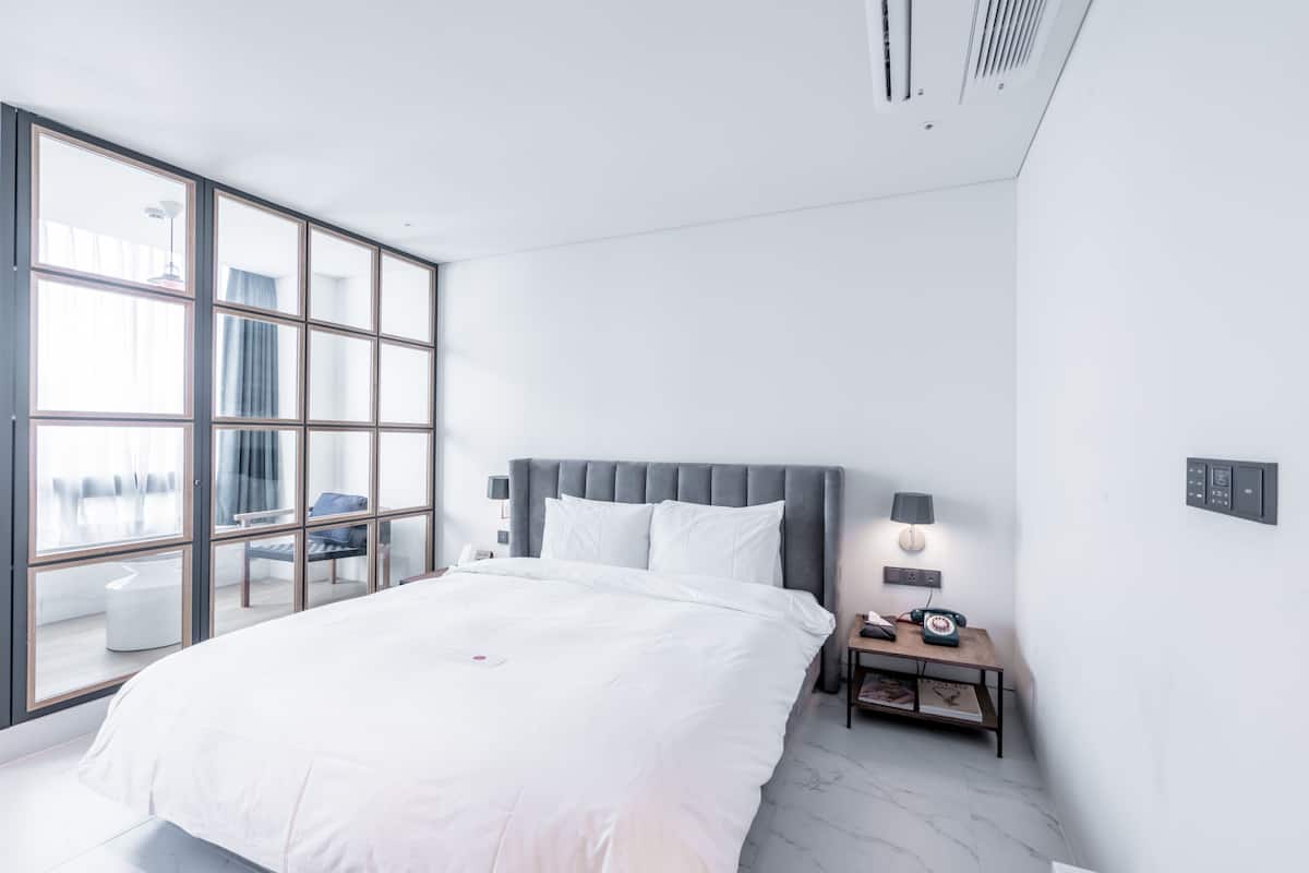 Un dormitorio moderno con una cama grande, una mesita de noche con lámpara y vistas amplias a través de ventanas de pared a techo.